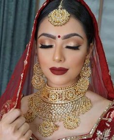 a woman in a red and gold bridal outfit with jewelry on her head, looking down