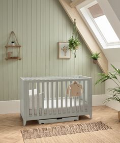 a baby crib in a room with green walls and wooden floors, along with a potted plant