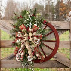 a christmas wreath on a wagon wheel with plaid bows and pine cones hanging from it