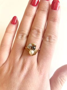 a woman's hand wearing a gold ring with two pearls and a black diamond