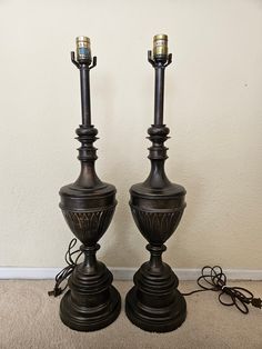 two metal lamps sitting next to each other on the floor in front of a wall