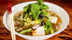 a white bowl filled with soup next to chopsticks on top of a wooden table