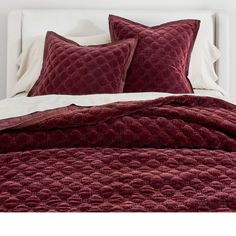 a bed that has some pillows on top of it and is covered in red blankets