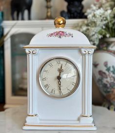 a white and gold clock sitting on top of a table next to a vase filled with flowers