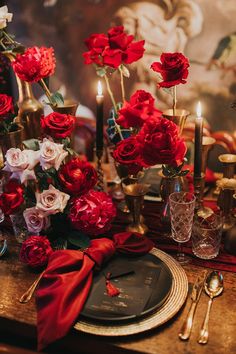 the table is set with red and white flowers in vases, silverware, and candles