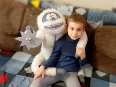 a young boy sitting on top of a bed next to a giant stuffed animal monster