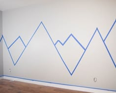 an empty room with blue tape on the wall and mountains painted on the wall behind it