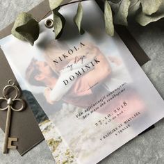 a wedding card with a key on it next to a bouquet of flowers and greenery