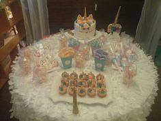 a table topped with lots of cupcakes and cookies on top of a white table cloth