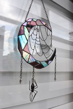 a stained glass wind chime hanging from a window with chain attached to the side