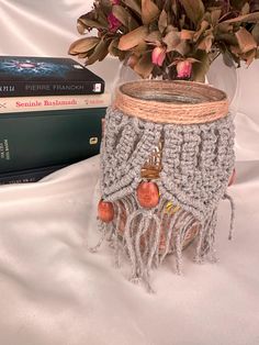 a crocheted vase with flowers in it next to a stack of books on a bed