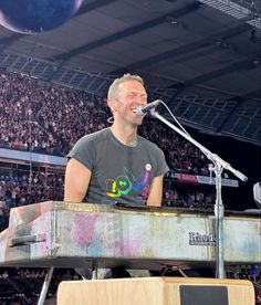 a man that is sitting at a keyboard in front of a microphone and some people