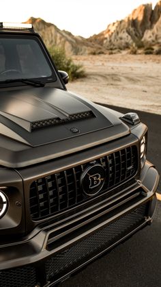 the front end of a black truck parked on top of a parking lot next to mountains