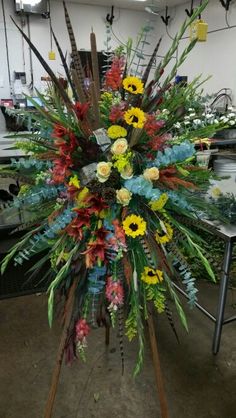 a large arrangement of flowers and plants on display in a room with other items behind it