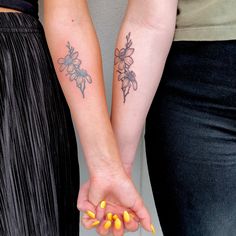 two women holding hands with yellow nails and tattoos on their arms, both wearing matching bracelets