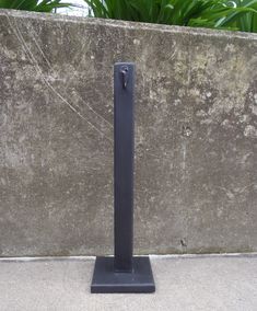 a tall black metal object sitting on top of a cement wall next to a plant