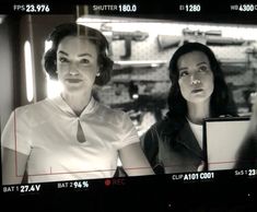 two women standing in front of a tv screen with the caption's name on it