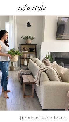 a woman standing next to a couch in a living room filled with furniture and plants