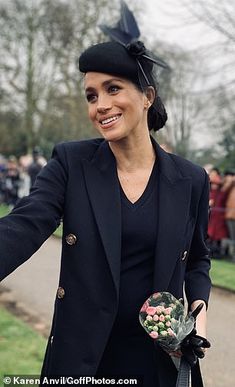 a woman wearing a black hat and holding flowers in her hand while walking down a path