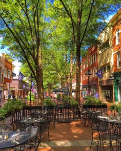 an outdoor dining area with tables, chairs and trees in front of buildings on a sunny day