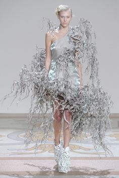 a model walks down the runway in a dress made out of tinsel and chains