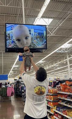 a man is holding up a baby in front of a television with an alien head on it