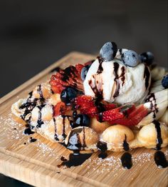 a wooden cutting board topped with fruit and ice cream covered in chocolate drizzle