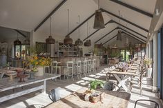 the inside of a restaurant with tables and chairs, potted plants and hanging lights