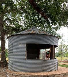 a round metal structure sitting in the middle of a field next to a large tree