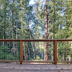 a wooden deck with metal railing and trees in the background