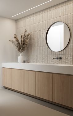 a bathroom with a round mirror above the sink next to a vase filled with flowers