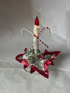 a candy cane is sitting on top of a christmas tree ornament with red and green leaves