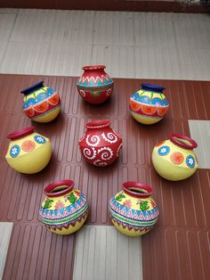 seven colorful vases sitting on top of a tile floor in front of a wall