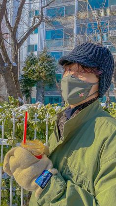 a person wearing a face mask and holding a drink in their hand while standing next to a fence