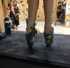 a person standing on top of a black mat in front of a climbing wall with other people