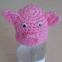 a pink knitted hat with eyes on top of a bottle