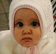 a baby wearing a white hat and pink scarf on top of it's head