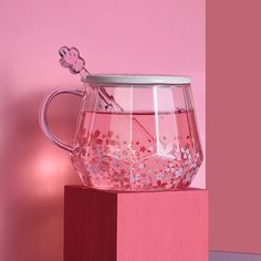 a pink vase with flowers on it sitting on top of a wooden block in front of a pink wall