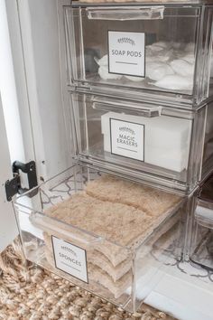 three clear drawers with labels on them in a closet filled with linens and other items