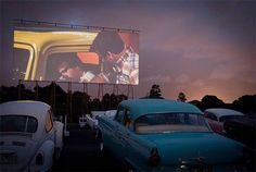 an old car parked in front of a movie screen