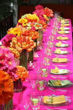 a long table is set with pink and orange flowers in vases, plates and silverware