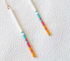 two necklaces that are sitting on a white surface, one is yellow and the other is pink