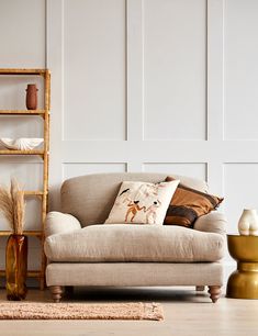 a living room scene with focus on the couch and pillows in the foreground, along with a shelf full of vases