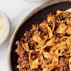 a bowl filled with pasta and meat on top of a white table next to two bowls