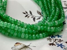 three strands of green glass beads sitting on top of a white and blue flowered plate