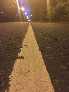 an empty street at night with the sun shining down on it and trees in the background