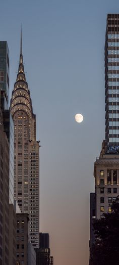 the moon is setting over skyscrapers in new york city