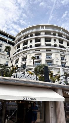 a tall white building with palm trees in front of it and people standing on the balcony