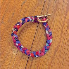 a colorful bracelet on a wooden floor with a gold hook in the center and two different colored braids around it