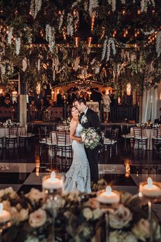 a bride and groom standing in front of candles at their wedding reception with greenery hanging from the ceiling